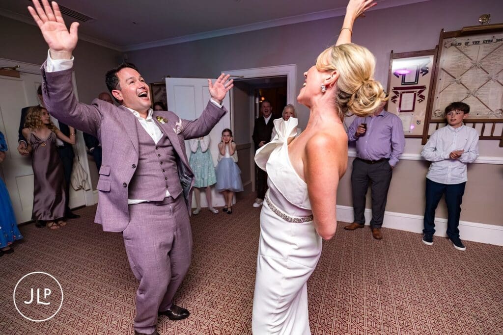 Joyful bride and groom dancing together with hands raised during their lively wedding reception party.