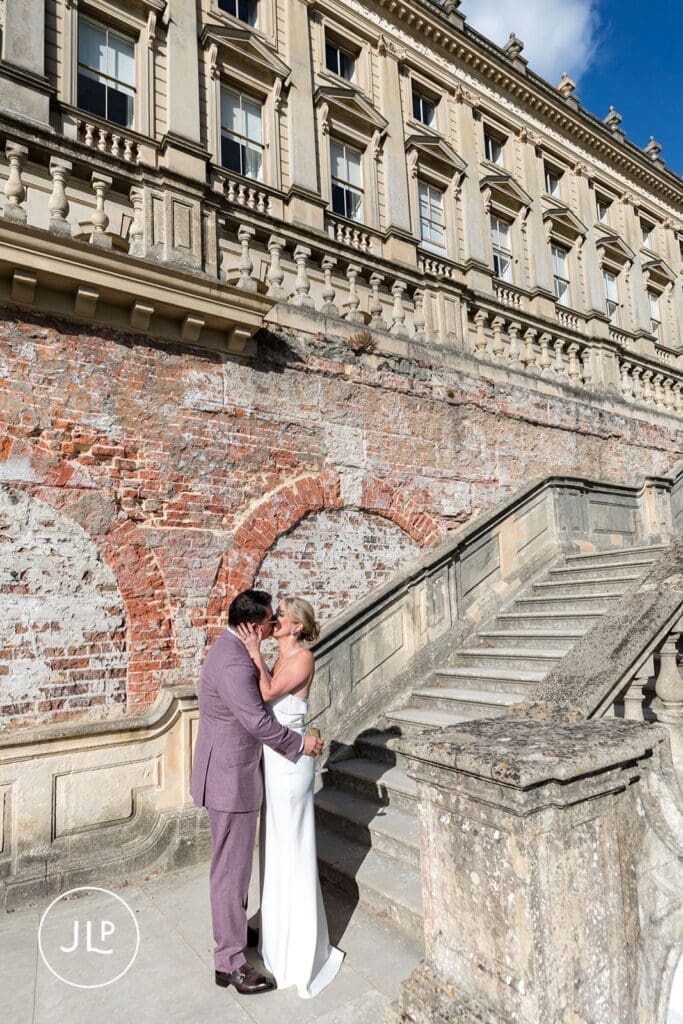 Bride and groom kissing by the grand stone staircase during their romantic Cliveden House wedding.