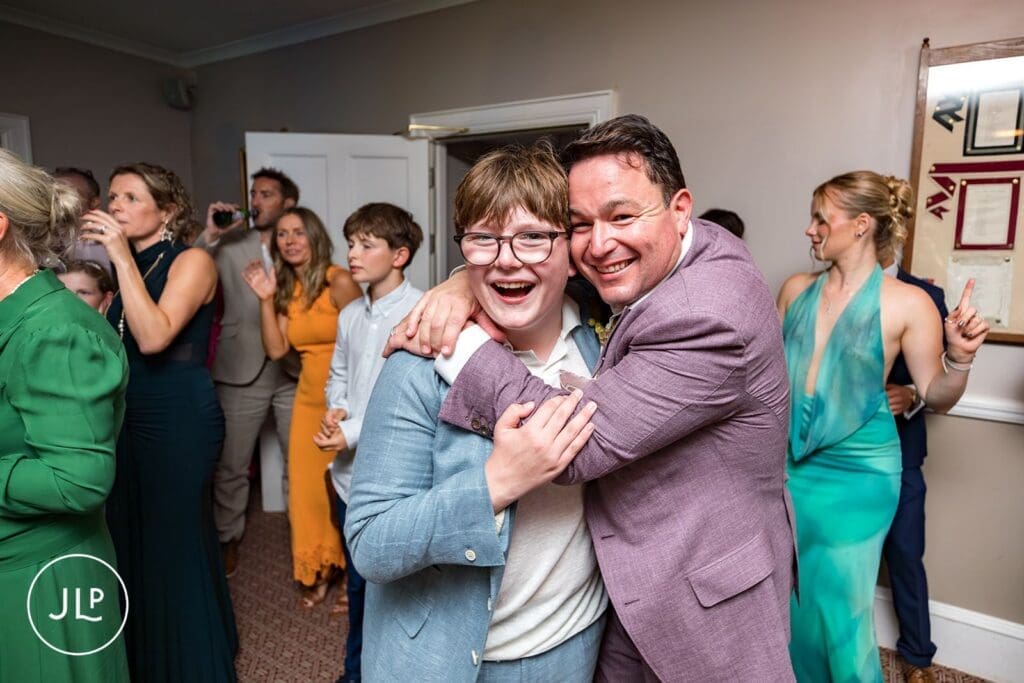 Groom smiling while hugging a young guest on the dance floor, captured by a documentary wedding photographer.