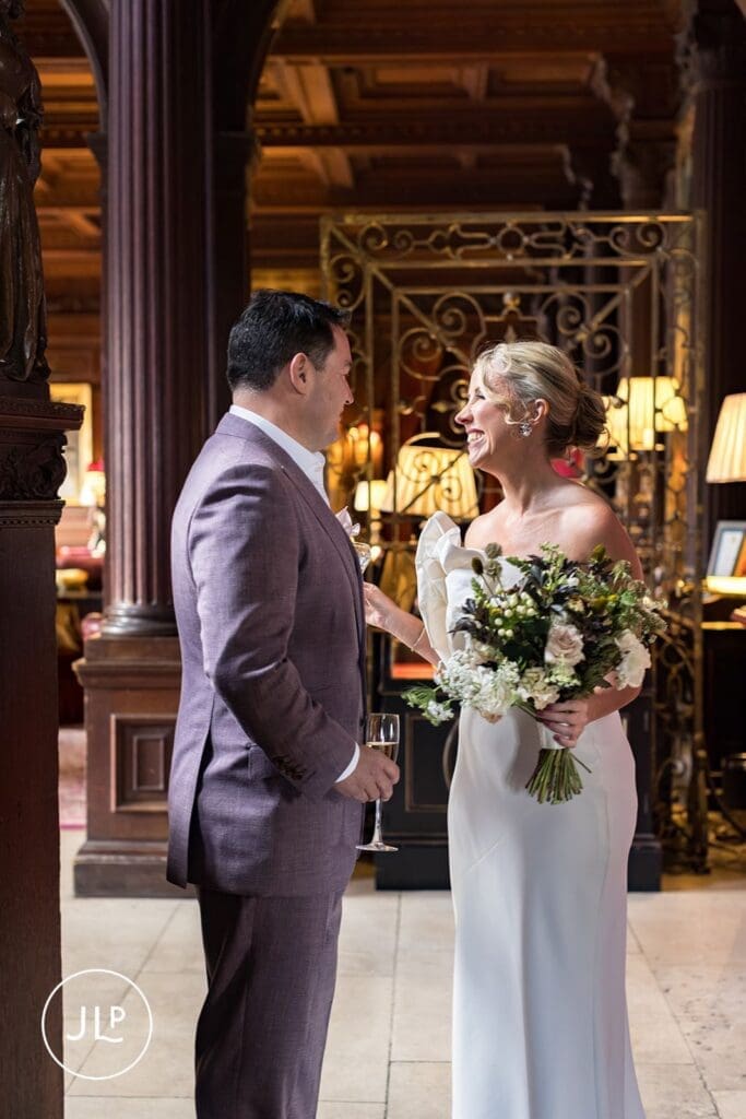 Smiling bride and groom holding champagne glasses inside a wood-panelled room during their Cliveden House wedding.