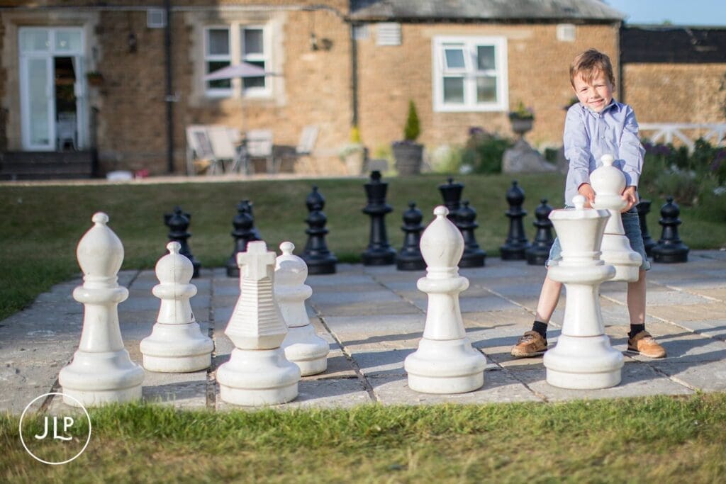 A young boy smiling while moving a large chess piece on an outdoor lawn