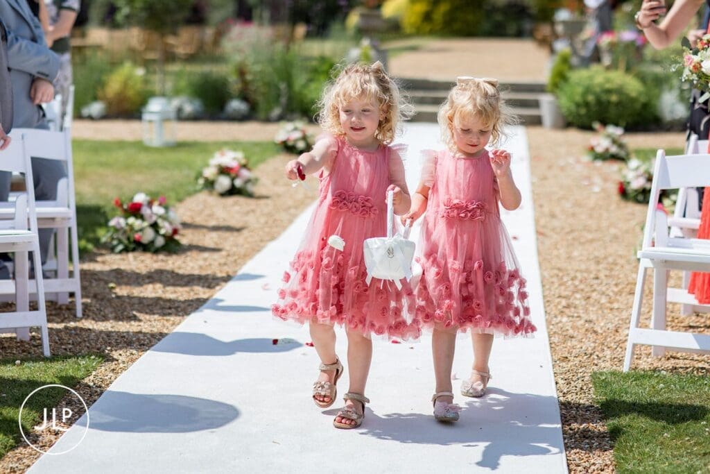 Two young flower girls in pink dresses walking the aisle, showcasing timeless natural wedding photography.