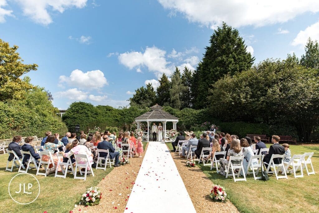 An outdoor garden ceremony at the white gazebo pavilion during sunny summer Hartsfield Manor weddings.