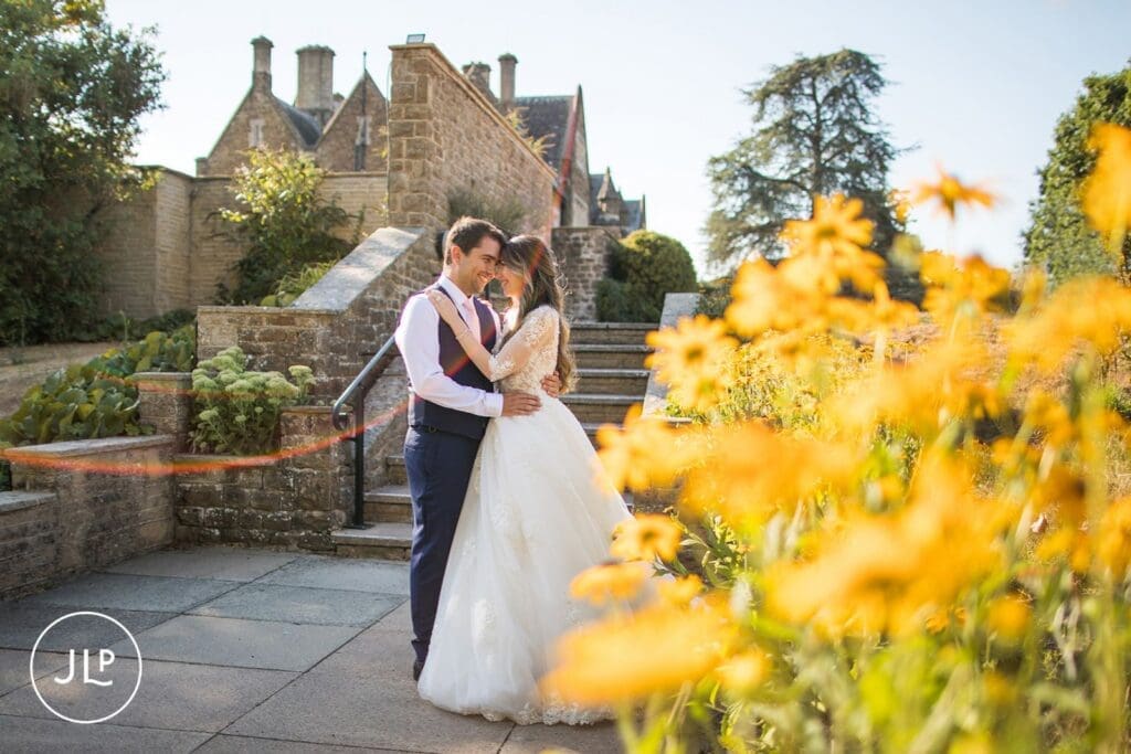 Bride and groom embracing behind bright yellow garden flowers during autumn Hartsfield Manor weddings.