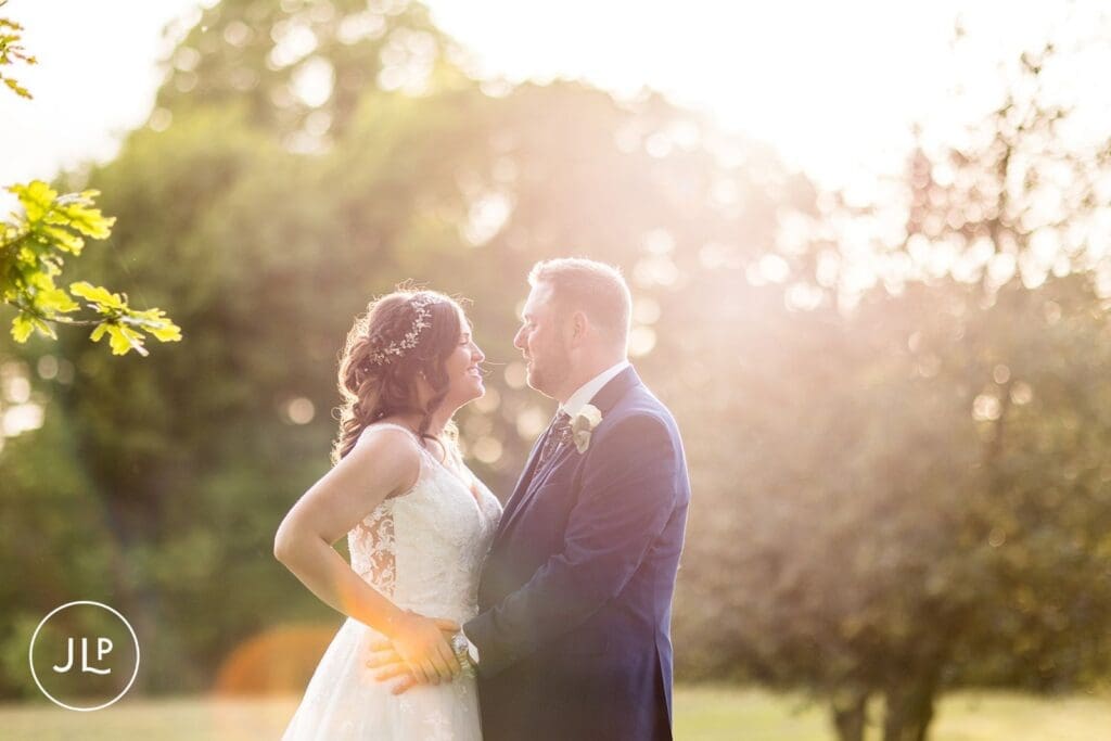 A sun-drenched outdoor portrait of a bride and groom embracing, by a Hartsfield Manor wedding photographer.
