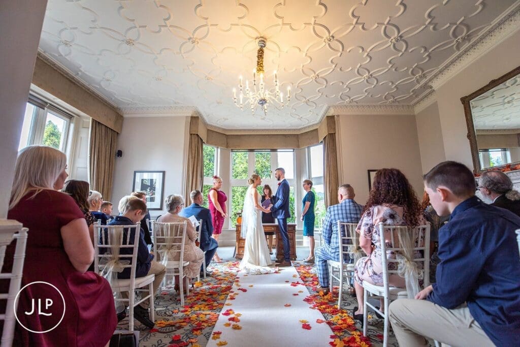 An indoor autumn ceremony with scattered leaves, detailed by an expert Hartsfield Manor wedding photographer.