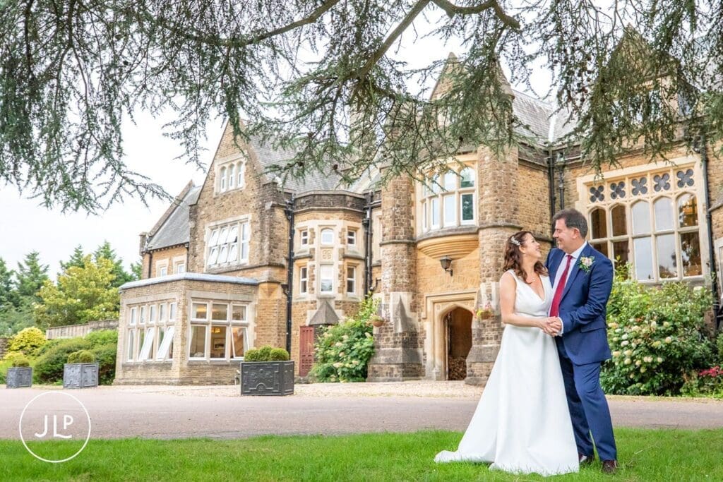 Newlyweds smiling on the lawns outside the grand manor house.