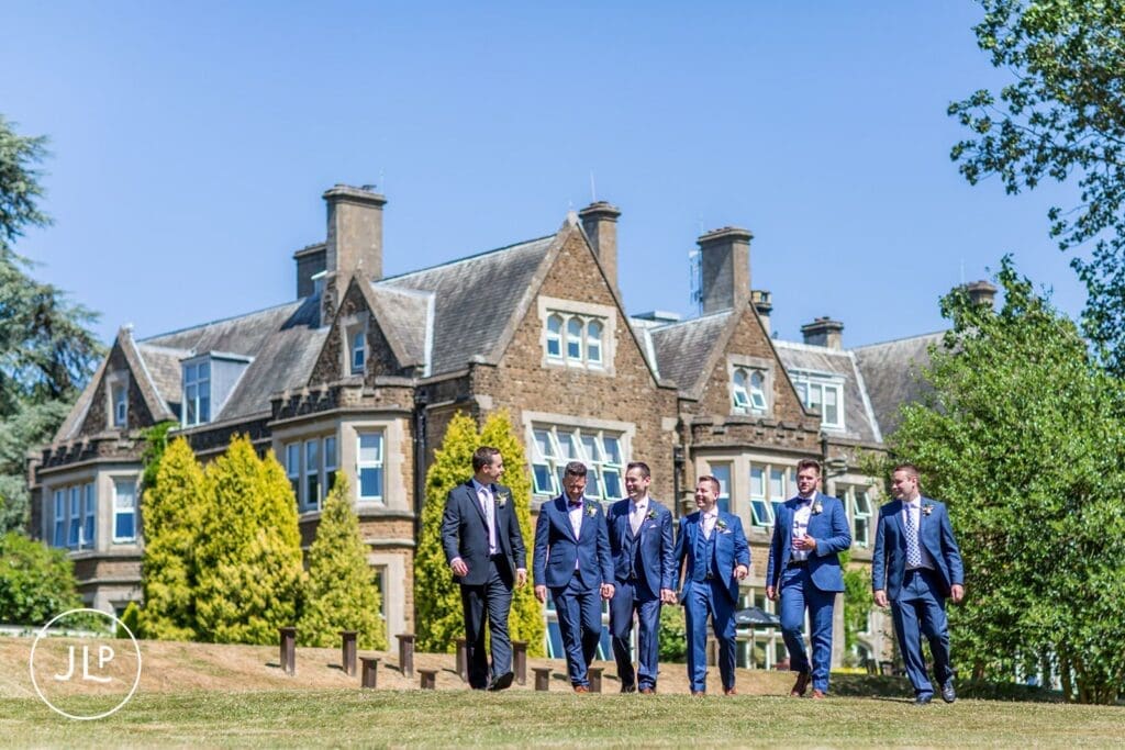 Groomsmen walking along the estate lawn, framed by a professional Surrey wedding photographer.