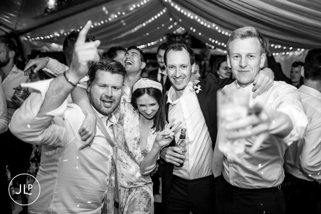 Candid of groomsmen and friends laughing during a luxury Surrey marquee wedding reception.