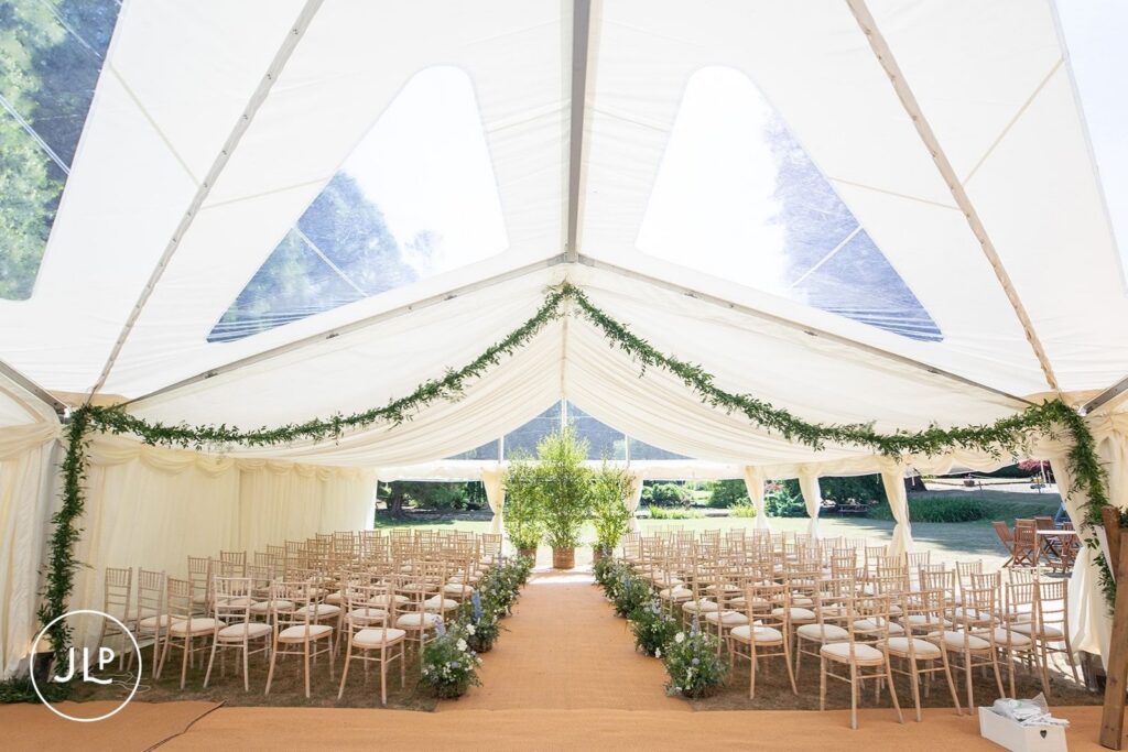 Elegantly styled interior of a luxury Surrey marquee wedding ceremony with floral aisle markers.