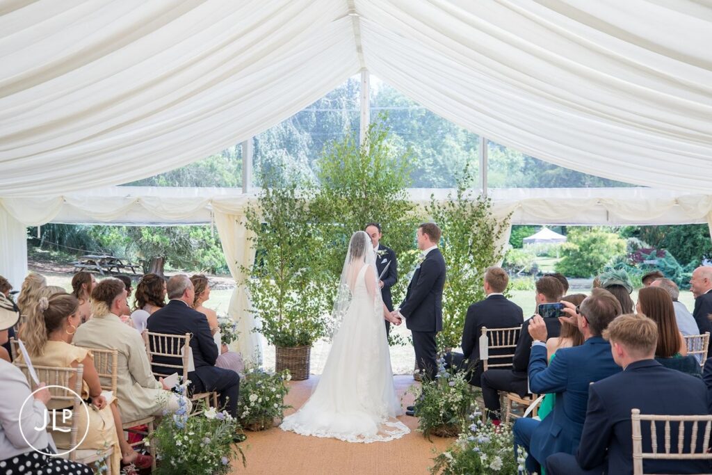 Wedding ceremony at a luxury outdoor wedding Surrey featuring natural tree backdrops inside the marquee.
