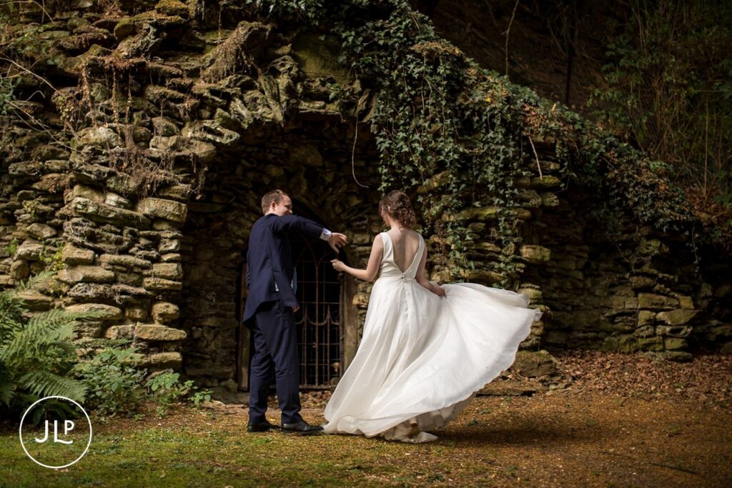Groom twirling the bride in front of a historic stone archway during marquee wedding photography UK.