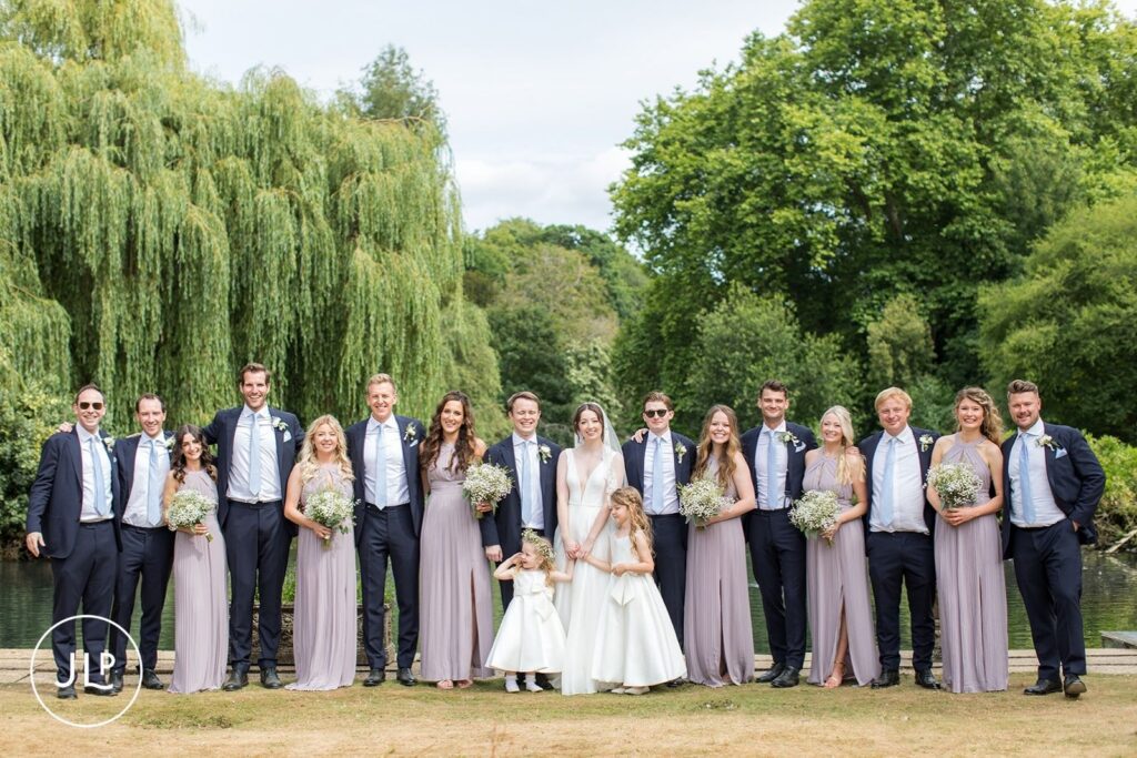 Full bridal party and groomsmen posing by the water for a luxury Surrey marquee wedding.