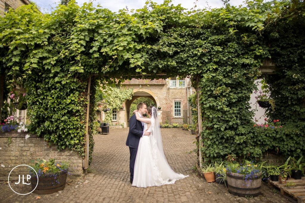 Romantic portrait of a bride and groom under an ivy-covered arch at a private estate wedding Surrey.