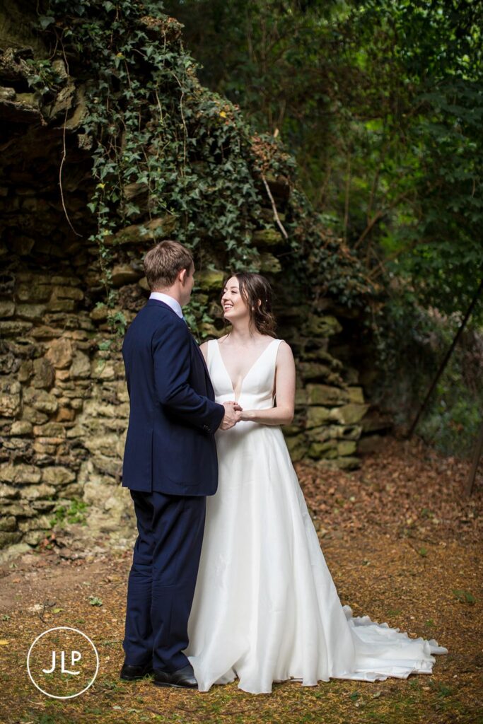 Newlyweds standing together in front of a rustic stone grotto, captured by a Surrey marquee wedding photographer.