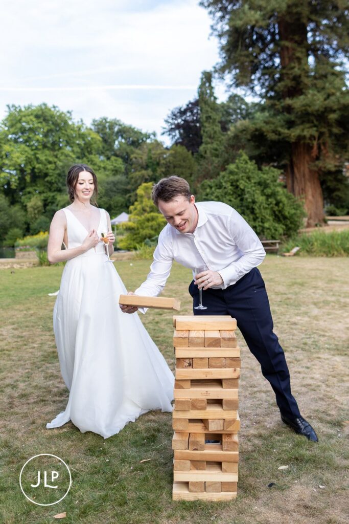 Bride and groom laughing while playing a game of giant wooden Jenga during an outdoor wedding reception.