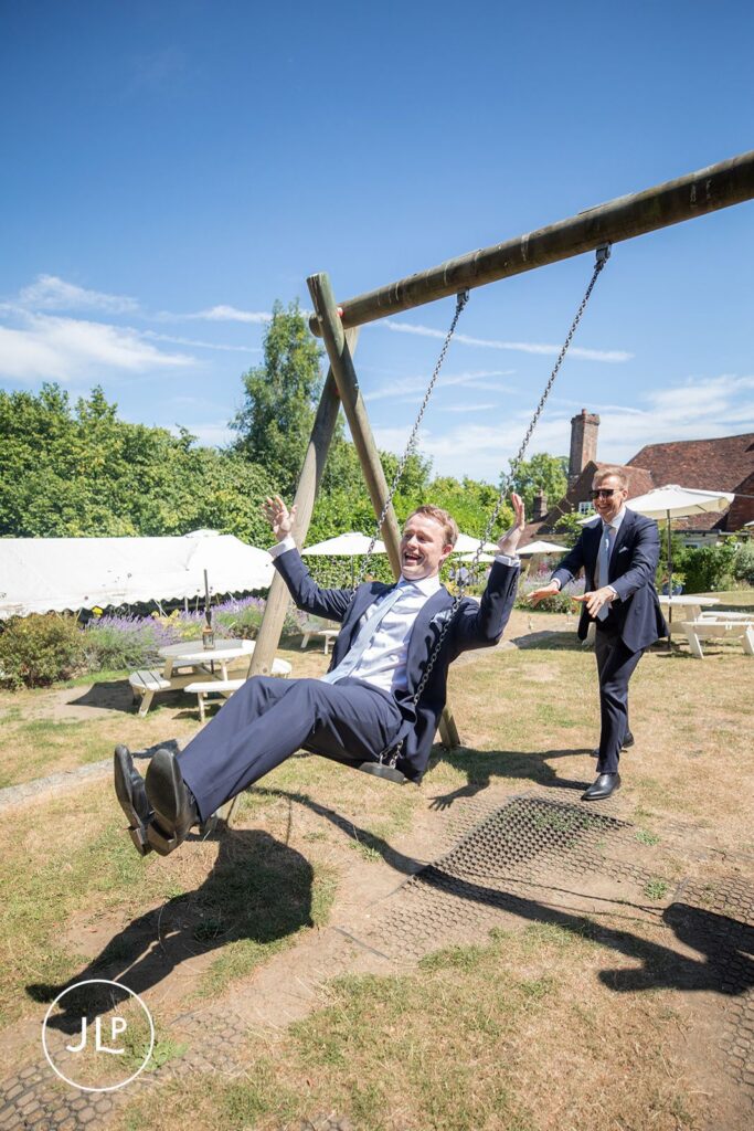 Playful shot of a groom on a swing during a luxury Surrey marquee wedding celebration.