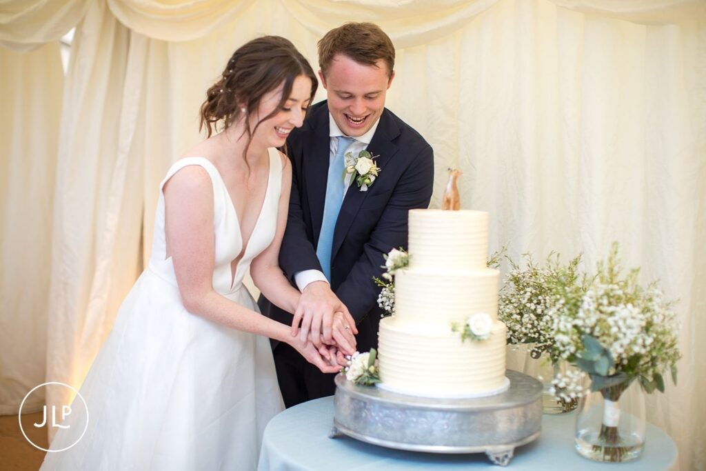 The joyful cake cutting moment captured by a Surrey marquee wedding photographer.