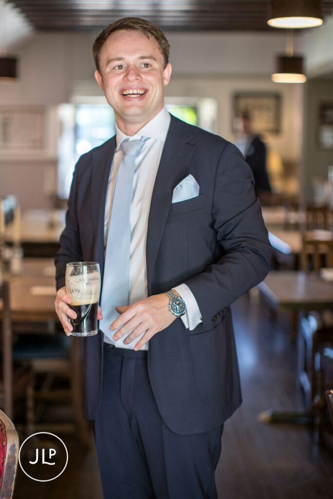 A happy groom holding a drink, captured by a Surrey marquee wedding photographer.