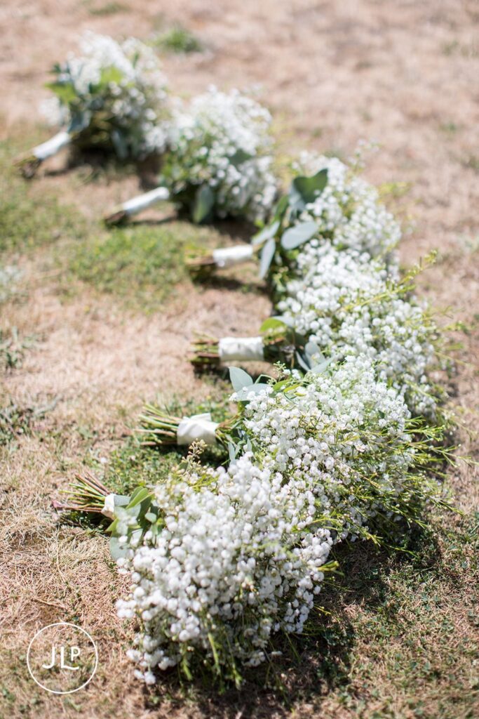 Row of baby's breath bridesmaid bouquets on grass, captured by a Surrey marquee wedding photographer.