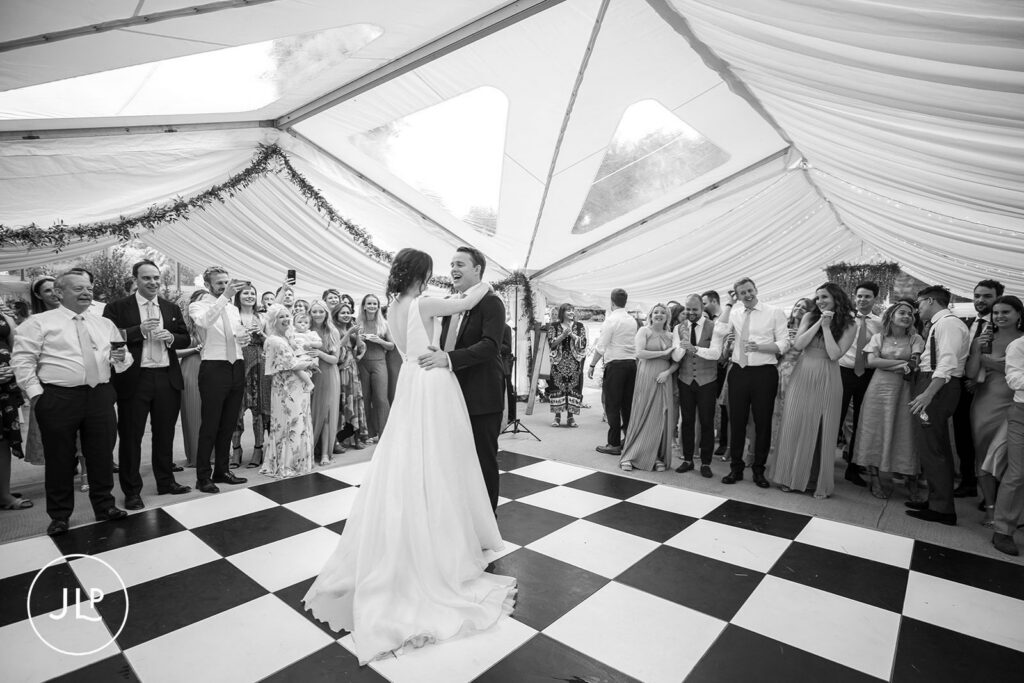 Black and white first dance on a checkered floor during a luxury Surrey marquee wedding.