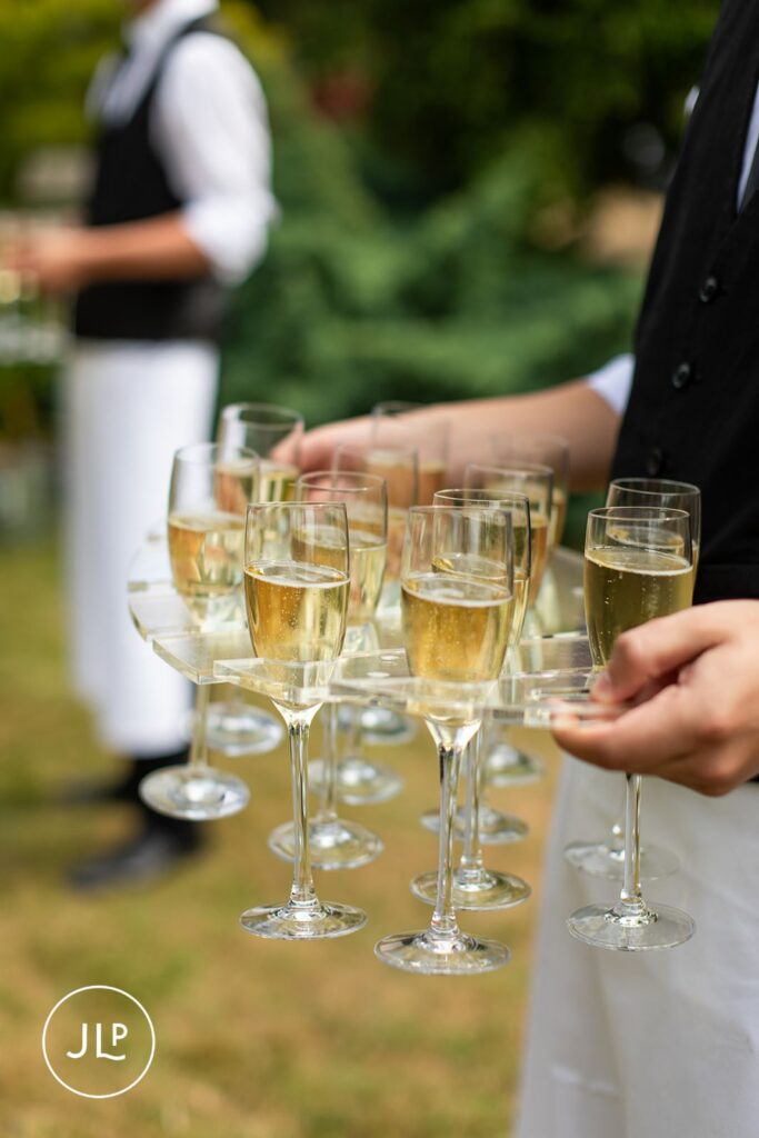 Server in a black vest carrying a clear acrylic tray filled with glasses of bubbling champagne.