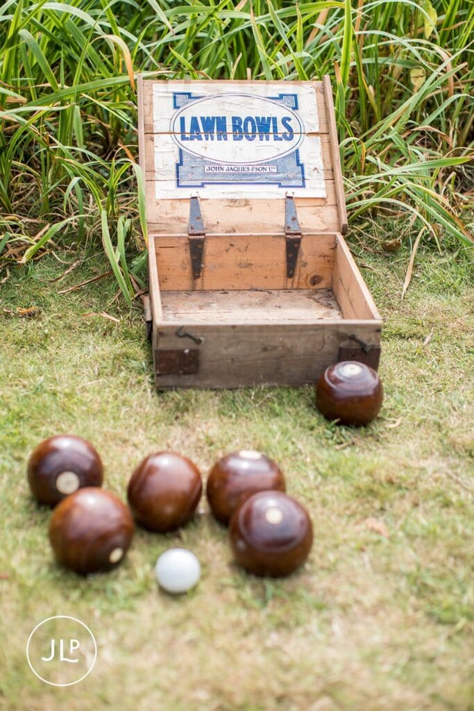 Vintage wooden crate labeled "Lawn Bowls" sitting on grass with brown bowls and a white jack.