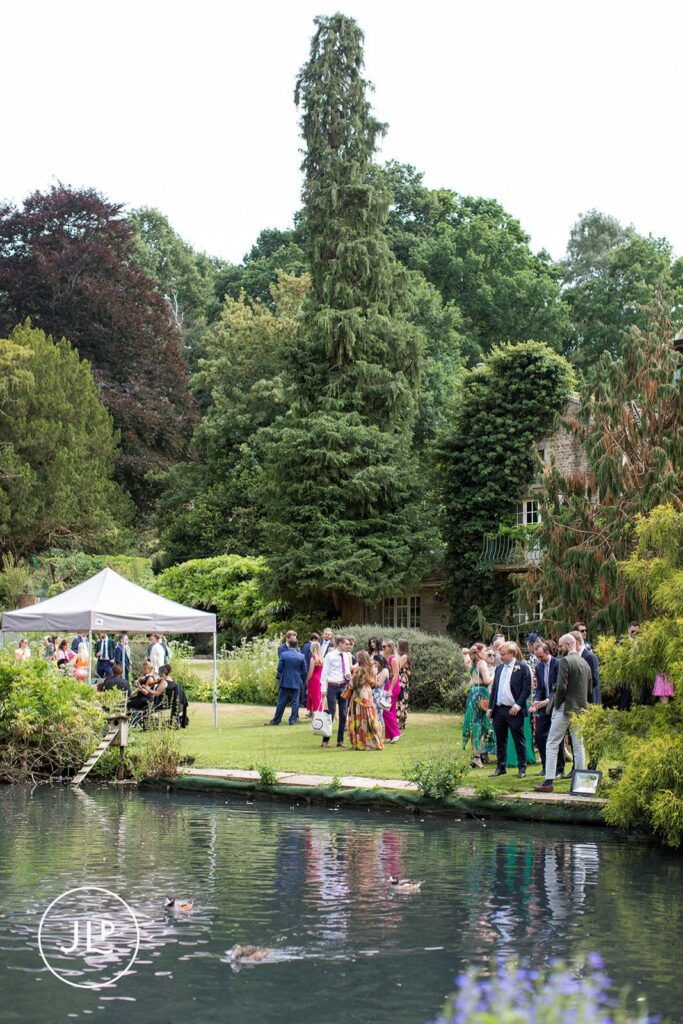 Wedding guests mingling on the lawn of a private estate wedding Surrey by a scenic pond.