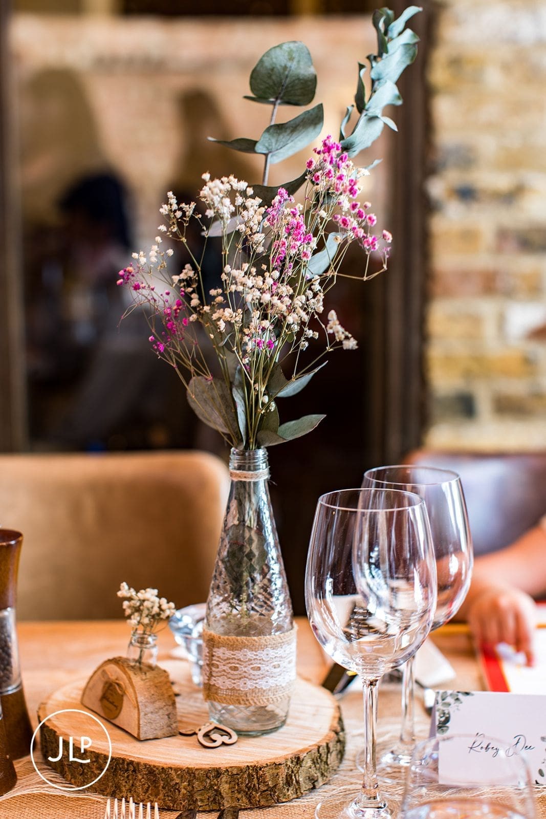 A rustic wedding table centerpiece featuring wildflowers in a lace-wrapped glass bottle on a log slice.
