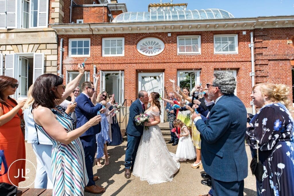 A newly married couple kisses under a cloud of bubbles blown by guests on the terrace outside York House.