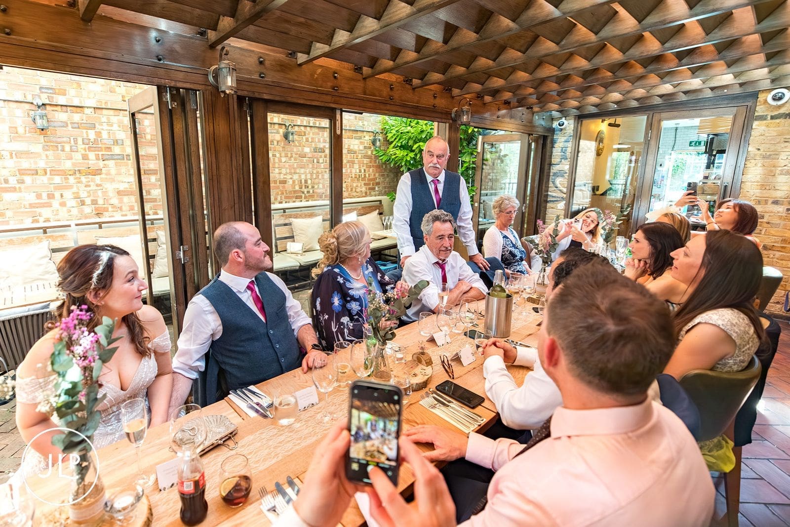 Wedding guests seated along a wooden table listen to speeches during a reception at York House.