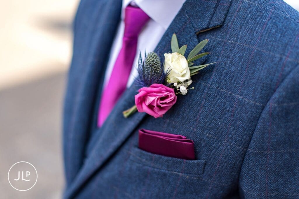 Close-up of a groom's blue tweed suit jacket and vibrant pink flower boutonniere at a London wedding.