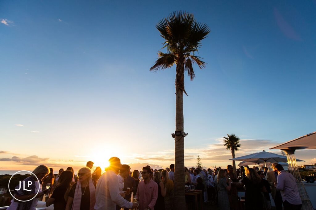 Golden hour silhouettes of guests at a luxury Algarve wedding party under a palm tree.