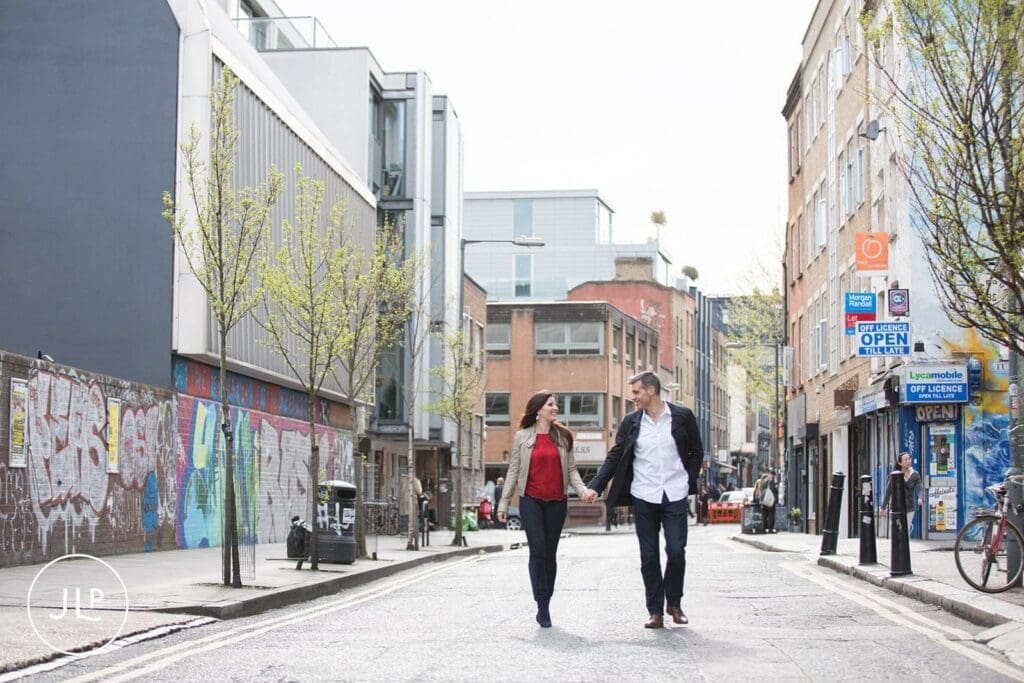 Couple holding hands while walking down a wide street for a relaxed East London engagement shoot.