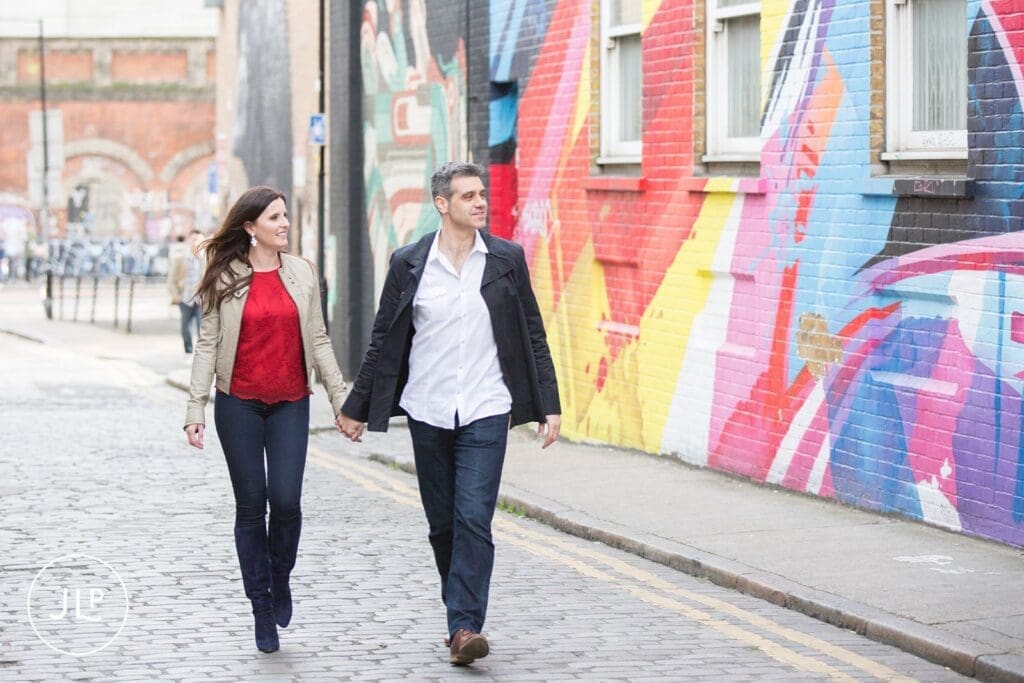 Smiling couple walking past bright murals, captured by an East London engagement photographer.