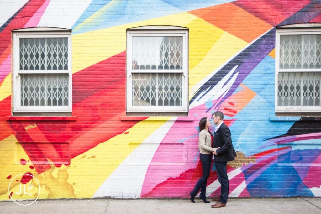 Couple embracing against a massive vibrant wall during their creative Brick Lane engagement shoot.