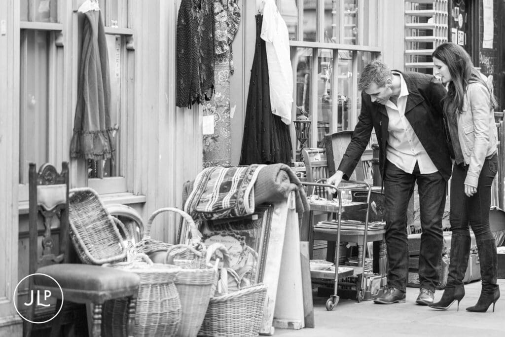 Black and white documentary engagement photography of a couple looking at vintage market stalls.