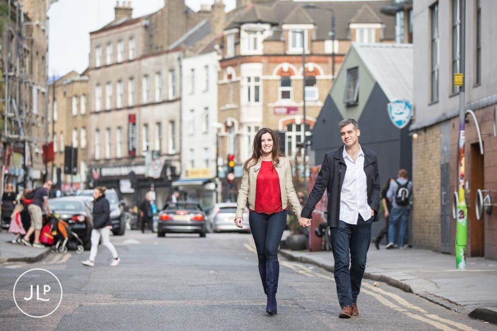 Couple holding hands while walking down a street for an East London engagement shoot.