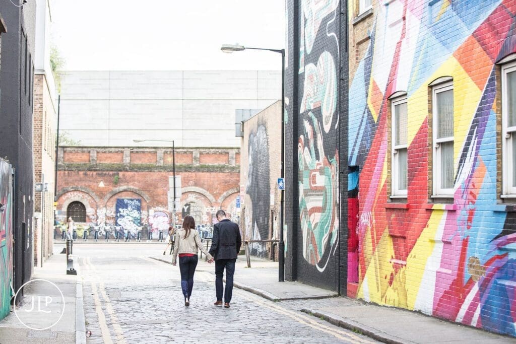 Couple walking away down a cobbled street during their Brick Lane engagement shoot.