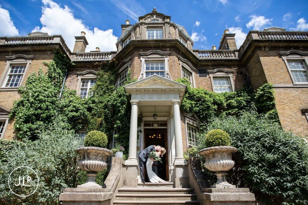 A newlywed couple kisses on the grand steps, photographed by a Hampton Court House wedding photographer.