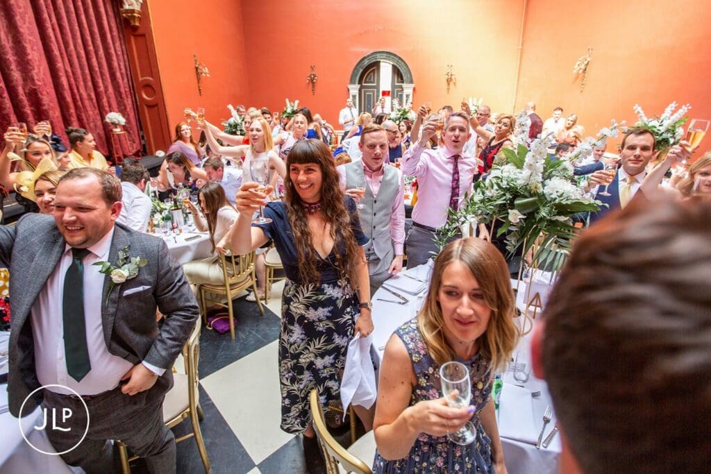 Lively wedding guest toast captured by an expert Hampton Court House wedding photographer during the reception.