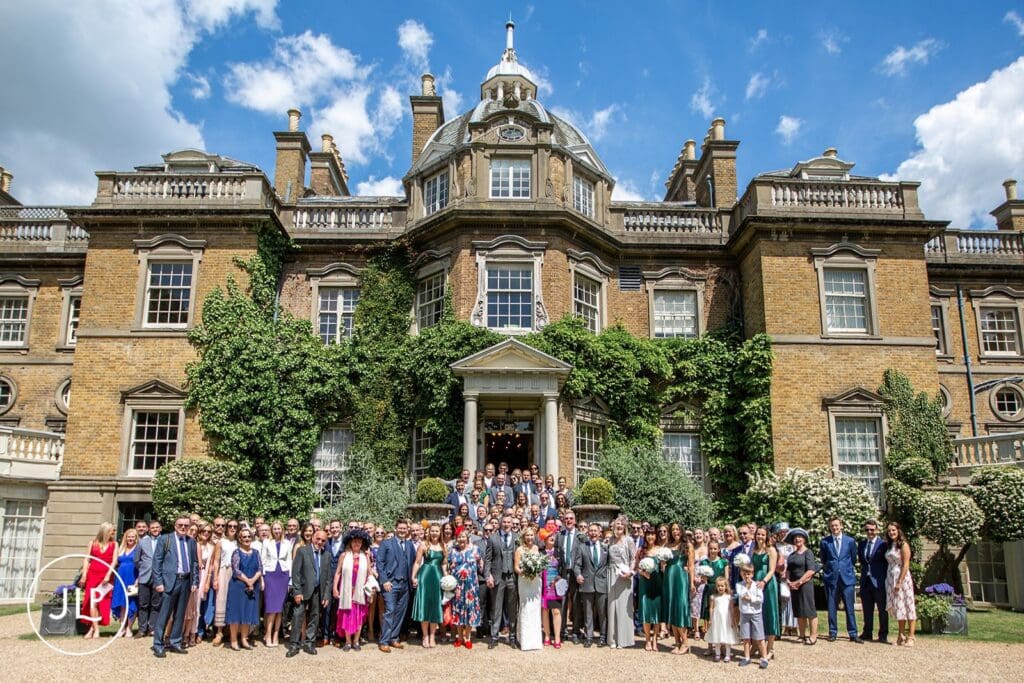 Wedding guests gather for a group photo outside Hampton Court House, an elegant Surrey wedding venue.