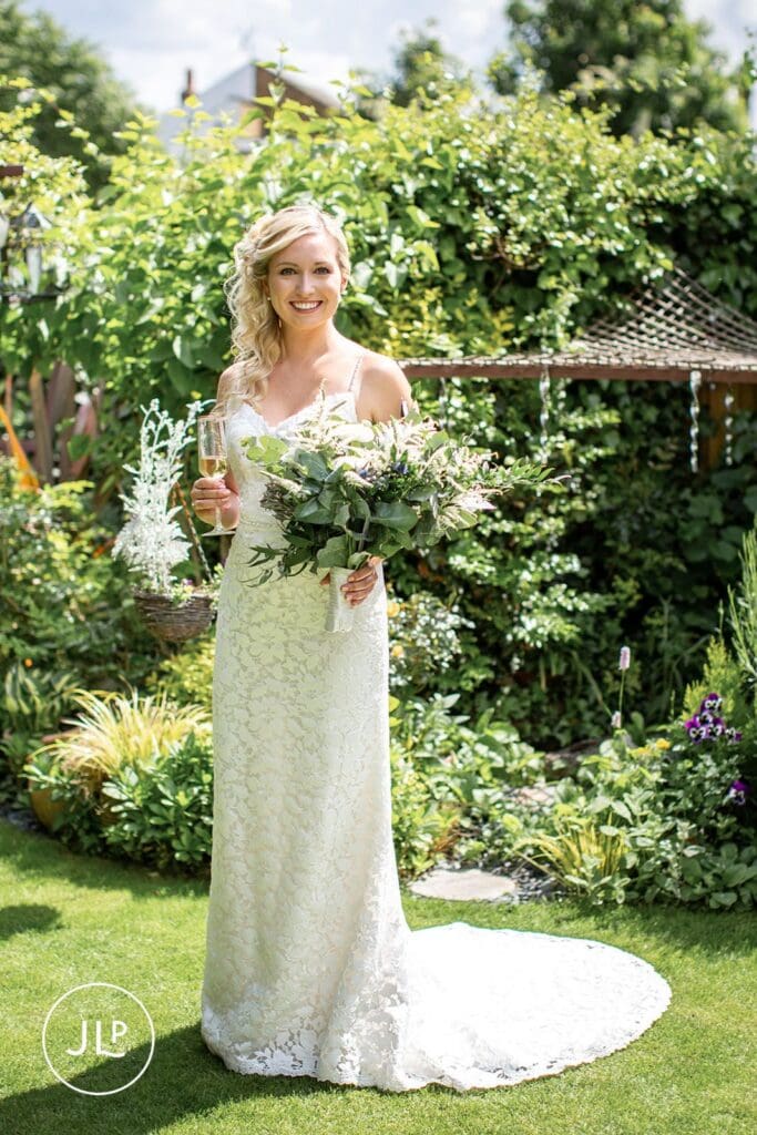 Smiling bride in lace dress holding bouquet, shot by a Hampton Court House wedding photographer.