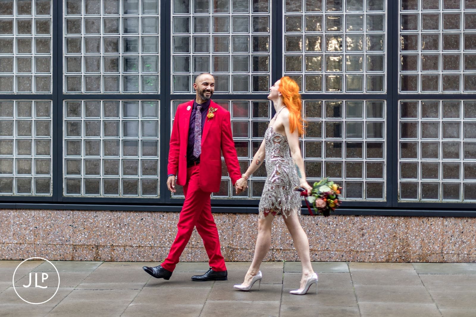 Bride in a beaded dress and groom in a red suit posing for modern urban nuptials portraiture.