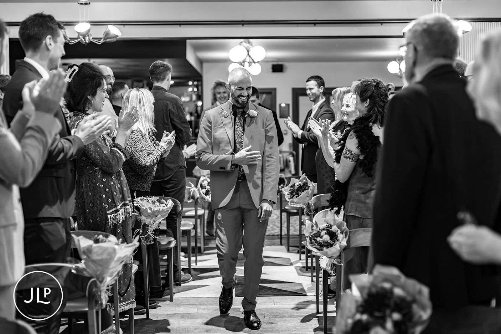 Groom in a suit smiling broadly while walking down the aisle at his central London wedding ceremony.