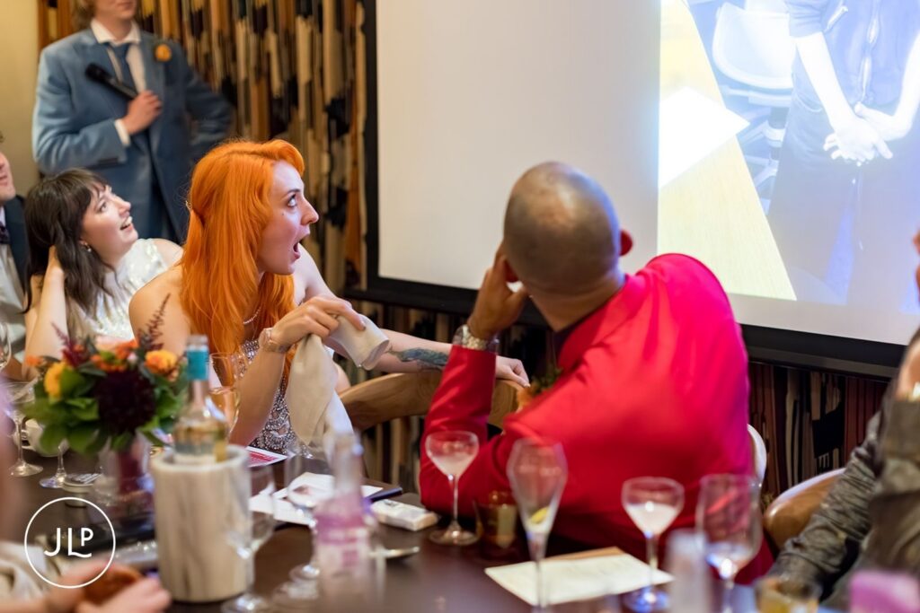 A candid moment of the bride reacting with surprise while looking at a presentation screen during the wedding dinner.