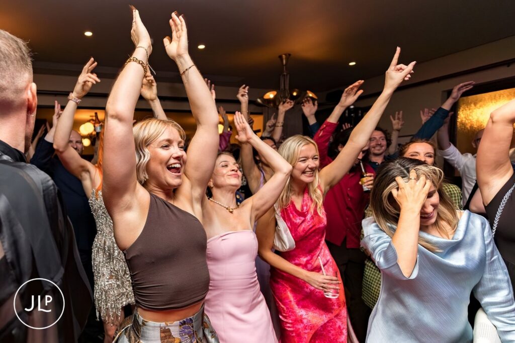 Documentary London wedding photographer captures guests cheering with hands up on a London wedding dance floor.