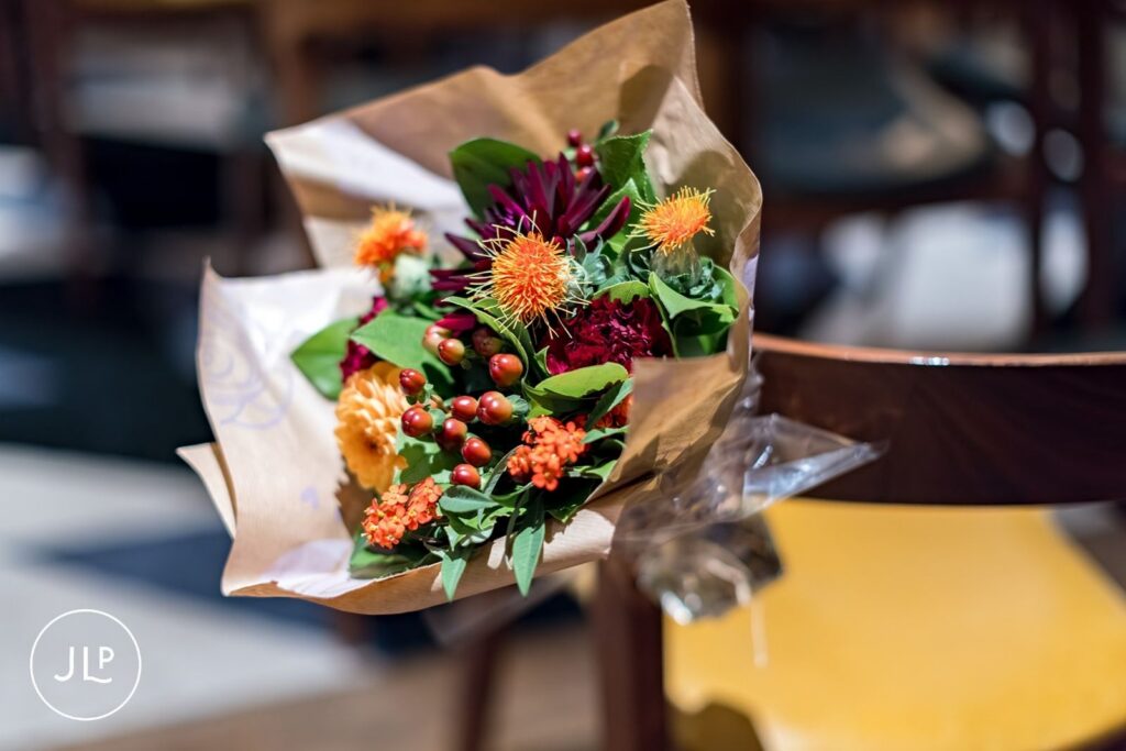 A colorful autumn wedding bouquet tied to a wooden chair with brown craft paper wrapping.