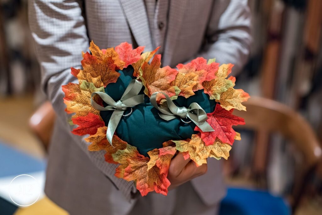A close-up of wedding rings on a heart-shaped pillow decorated with colorful autumn maple leaves.