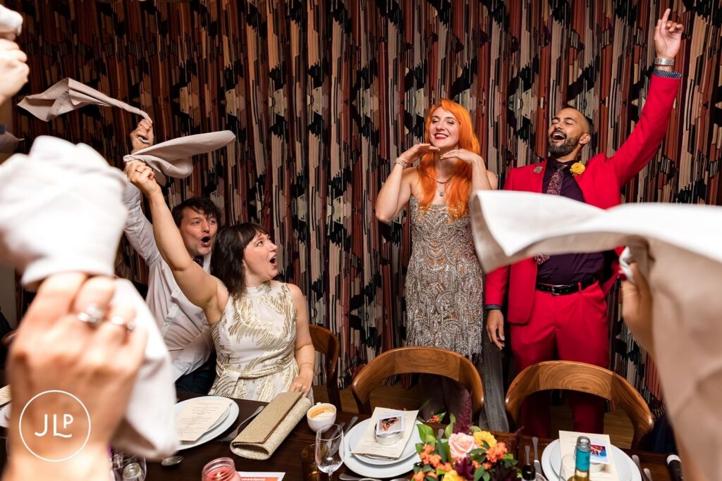 The bride and groom laughing and cheering with their guests as they wave white napkins during the reception party.